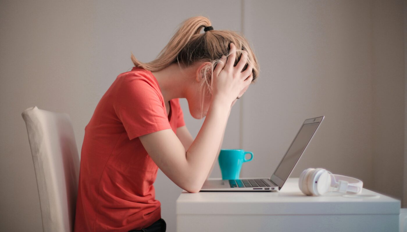 Young woman feeling stressed while studying at home with a laptop and coffee cup.