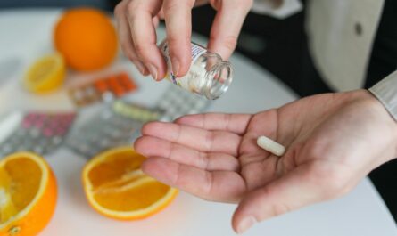 Close-up of a person taking a vitamin capsule with citrus fruit and medication on a table.
