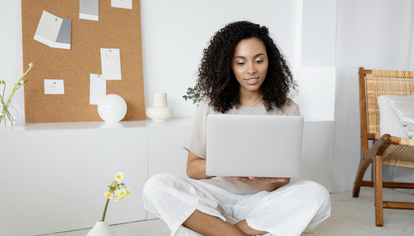 Young woman with curly hair working on her laptop in a cozy home setting, exuding confidence and focus.